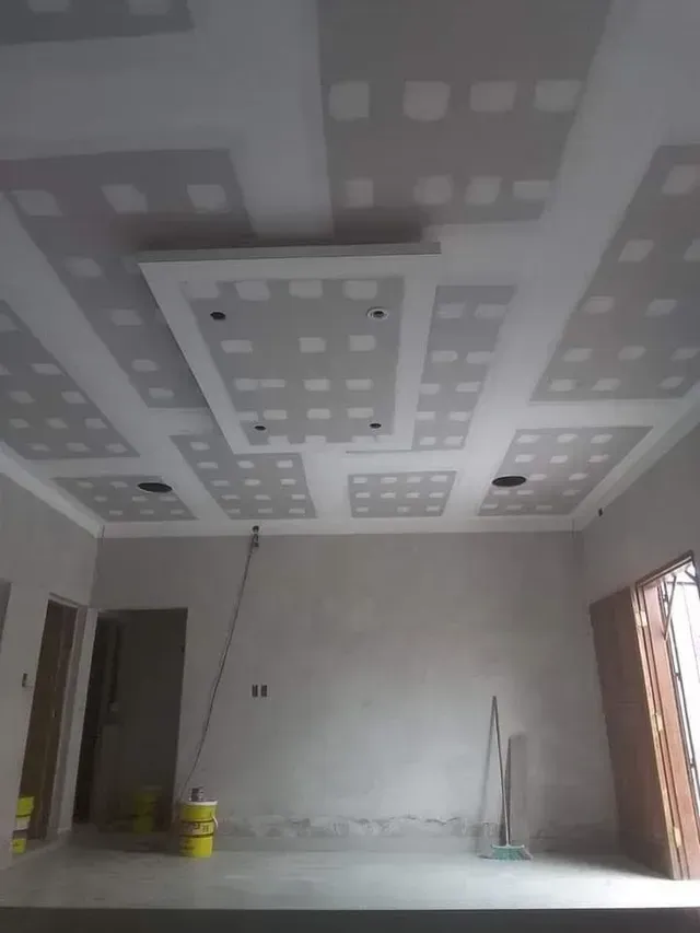 Habitación sin terminar con parches en el techo de pladur, paredes grises y herramientas en el suelo.