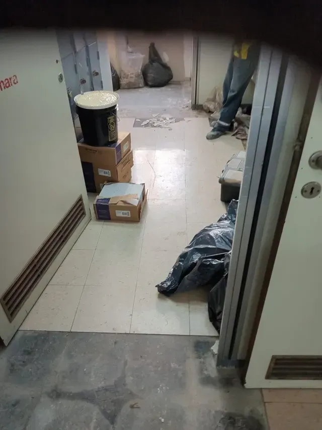 Pasillo estrecho con cajas, bolsas de basura y una persona de pie cerca de una puerta abierta.