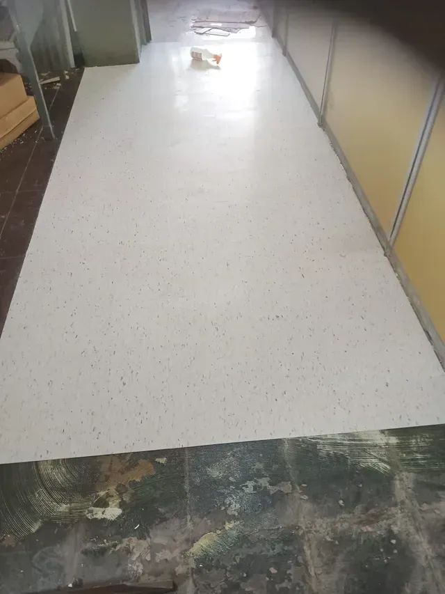 Pasillo estrecho con suelo blanco y paredes beige, que conduce a una puerta luminosa al final.