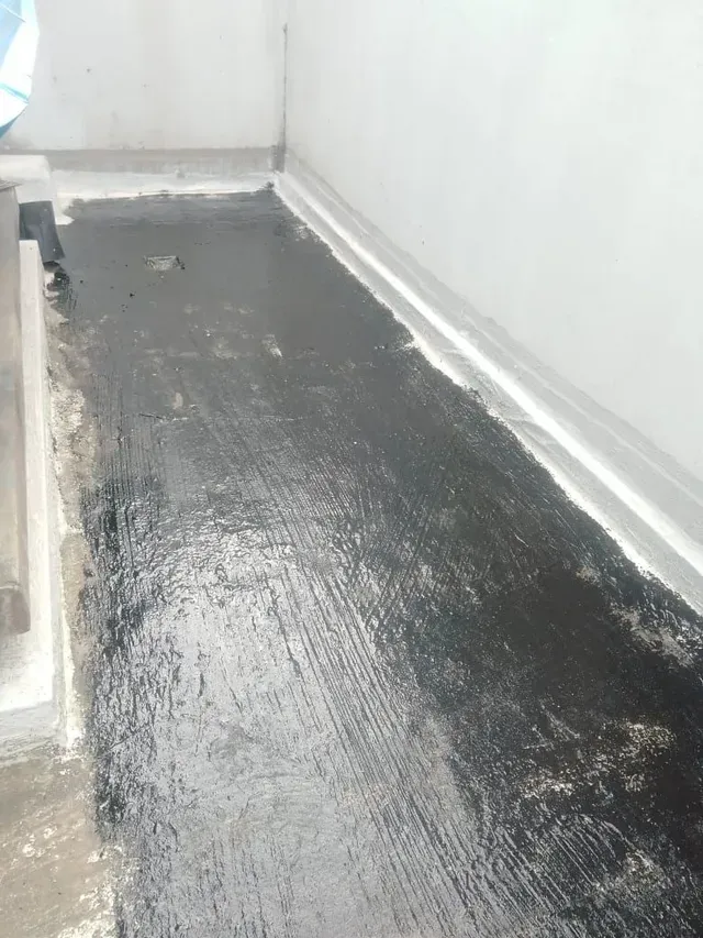 Suelo negro recién pintado en un estrecho pasillo blanco o zona de balcón con algunas zonas rugosas cerca de las paredes.