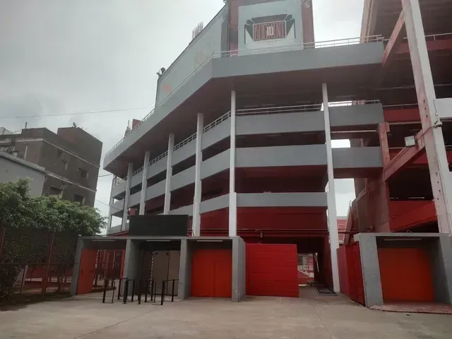 Edificio moderno de varias plantas con columnas blancas y detalles rojos bajo un cielo nublado.