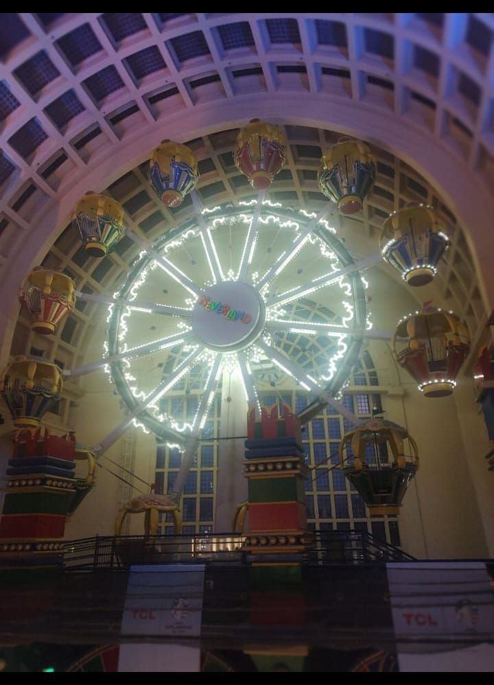 Una noria iluminada en el interior, bajo un techo abovedado, con coloridas góndolas a su alrededor.