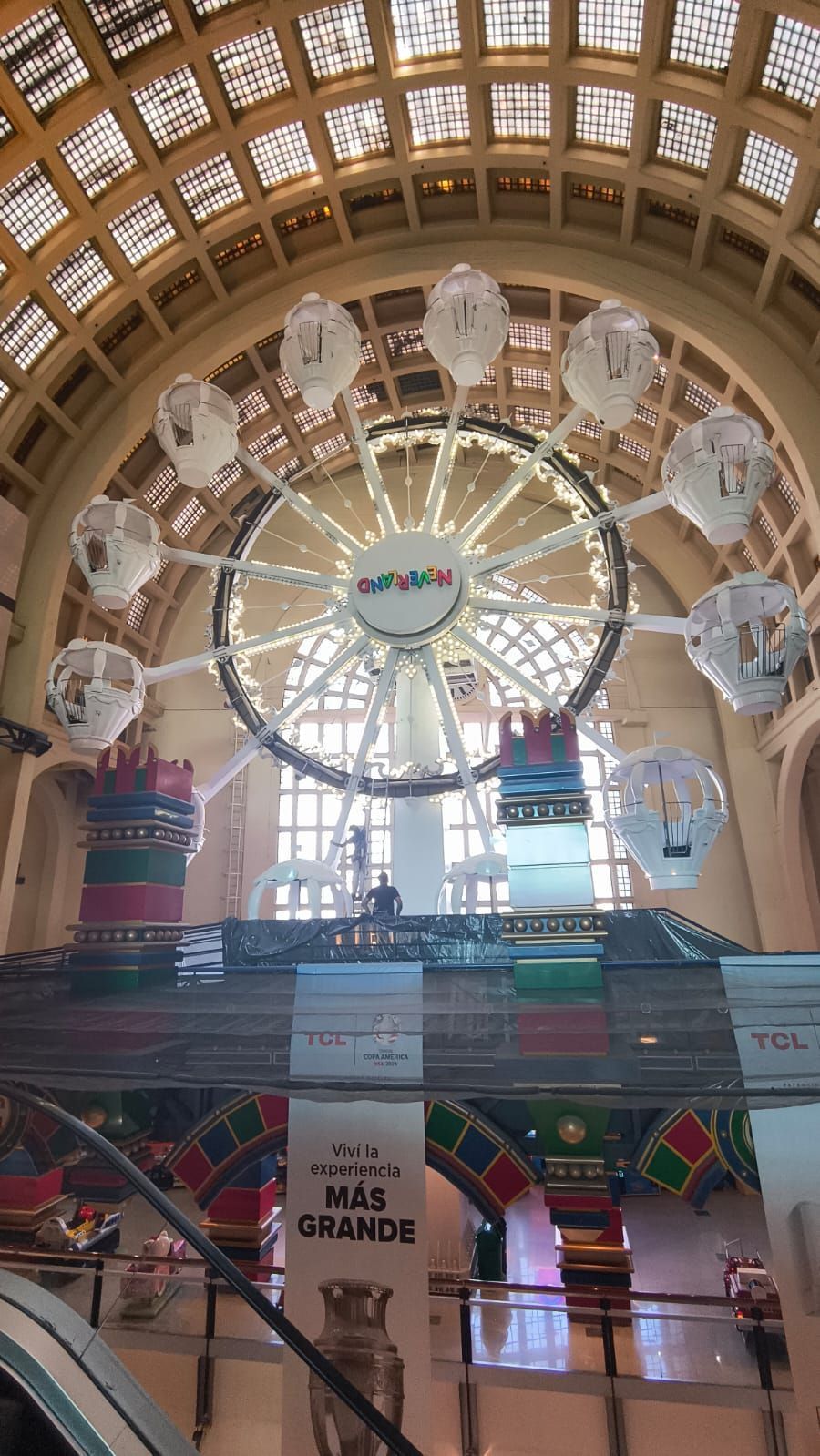 Gran salón interior con una gran noria y arcos festivos bajo un techo abovedado.