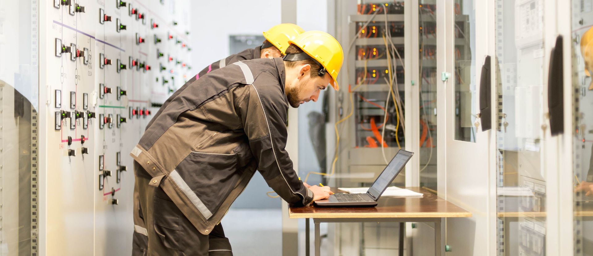 a man in a hard hat is using a laptop computer in an electrical room .