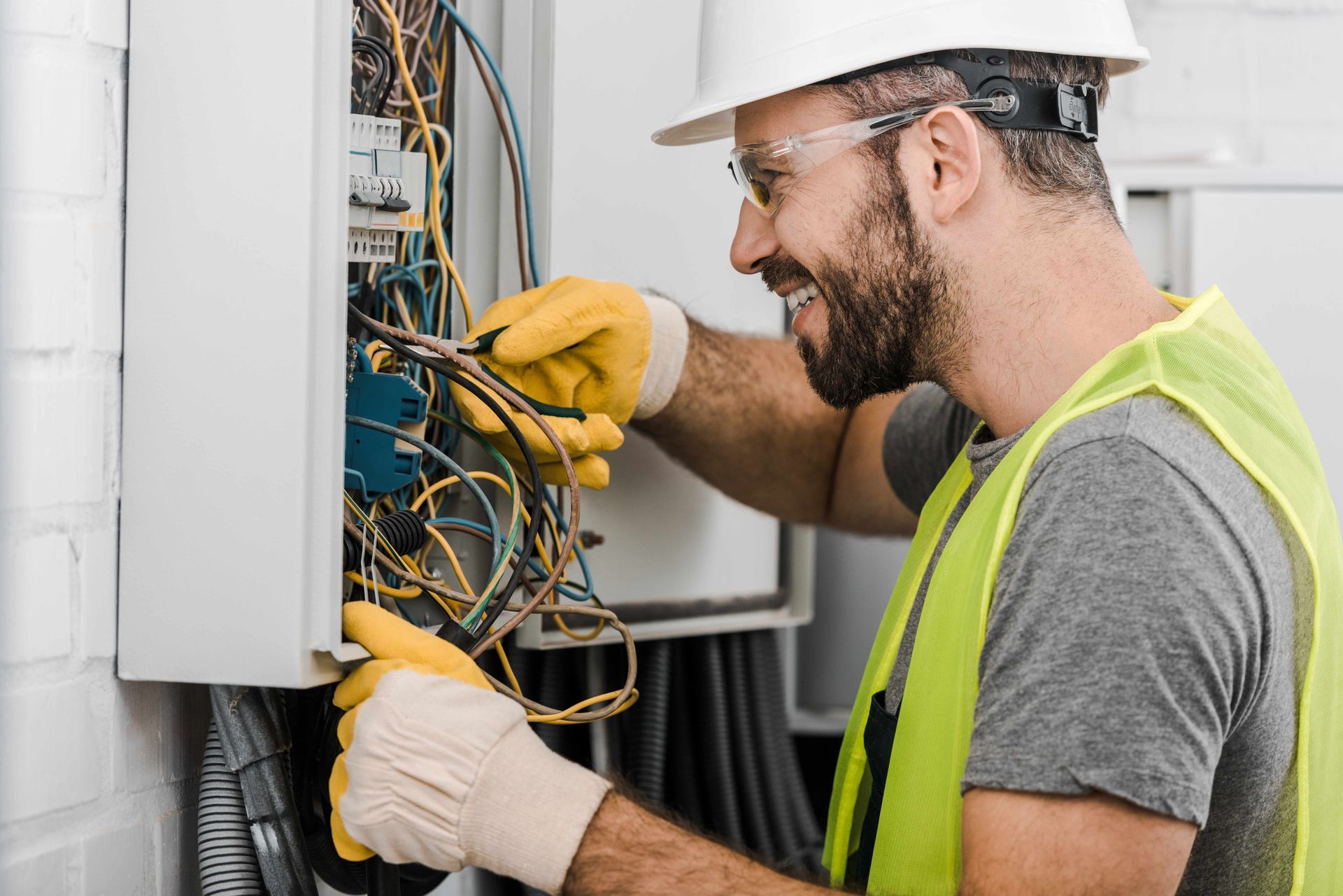 a man in a hard hat and safety vest is working on an electrical box .