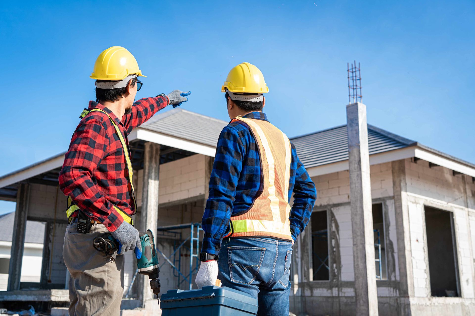 two construction workers are standing in front of a house under construction .