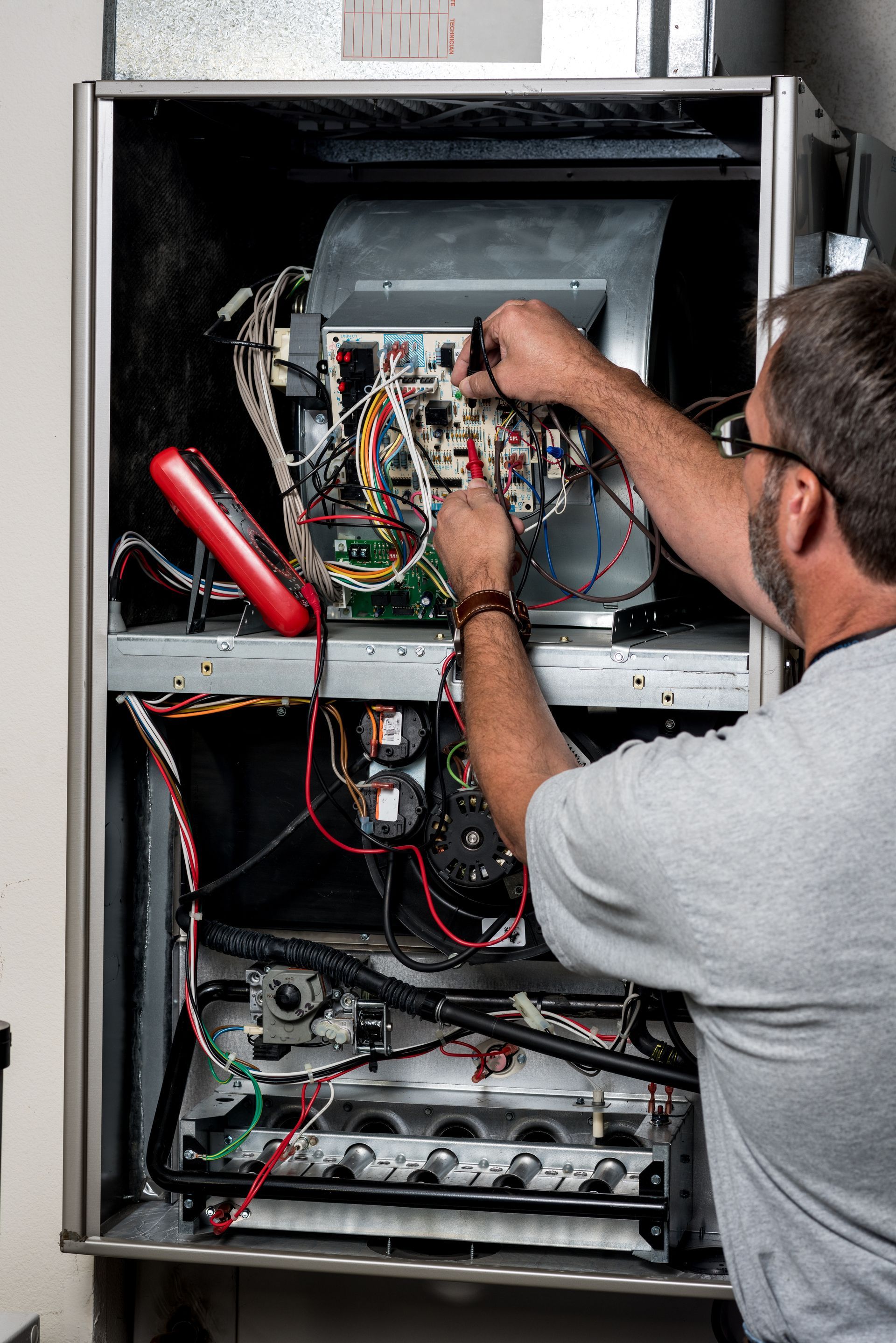 Mechanic works on a home furnace with volt meter Mechanic works on a home furnace with volt meter