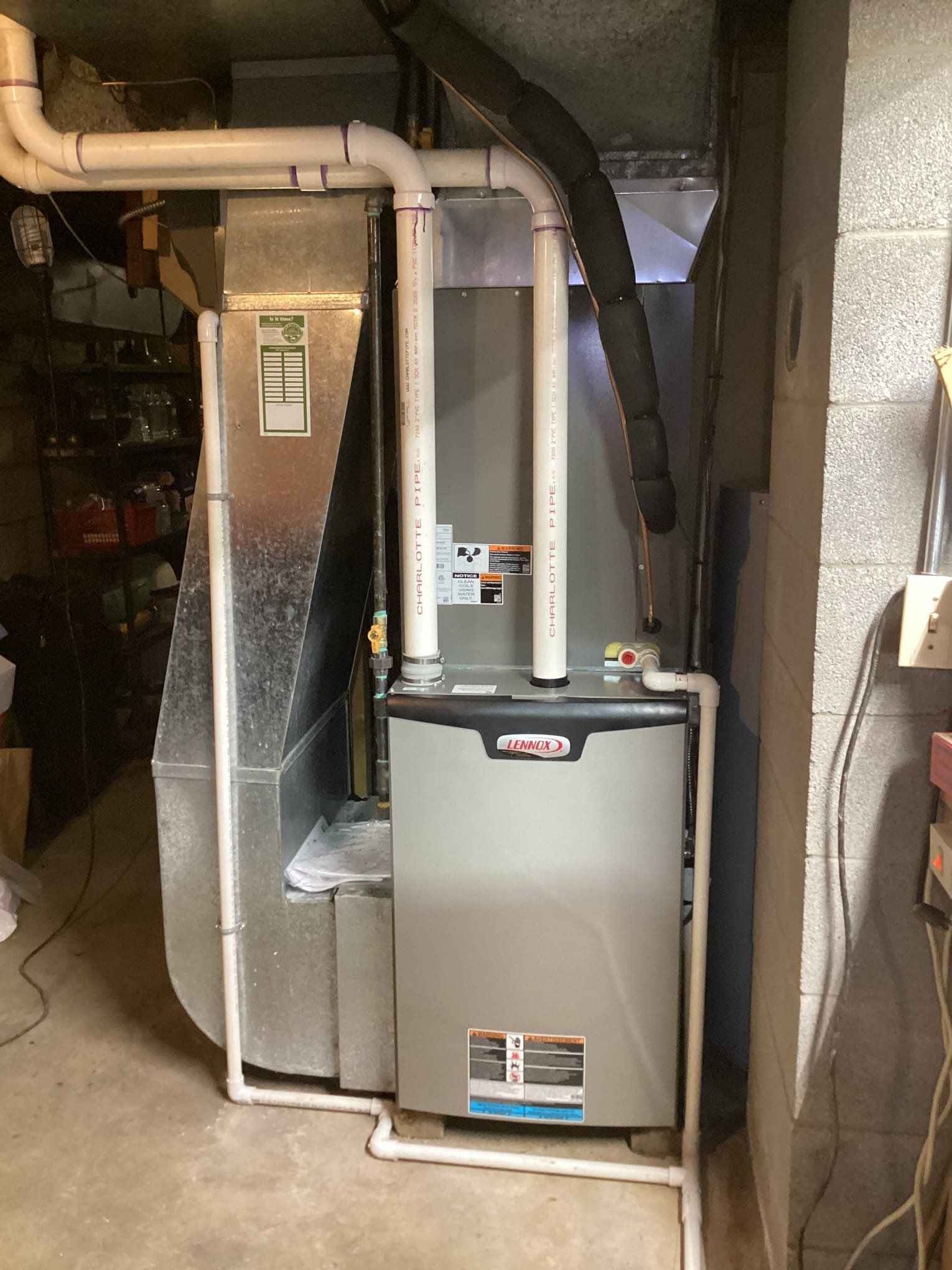 An air conditioner is sitting in a basement next to a pipe.