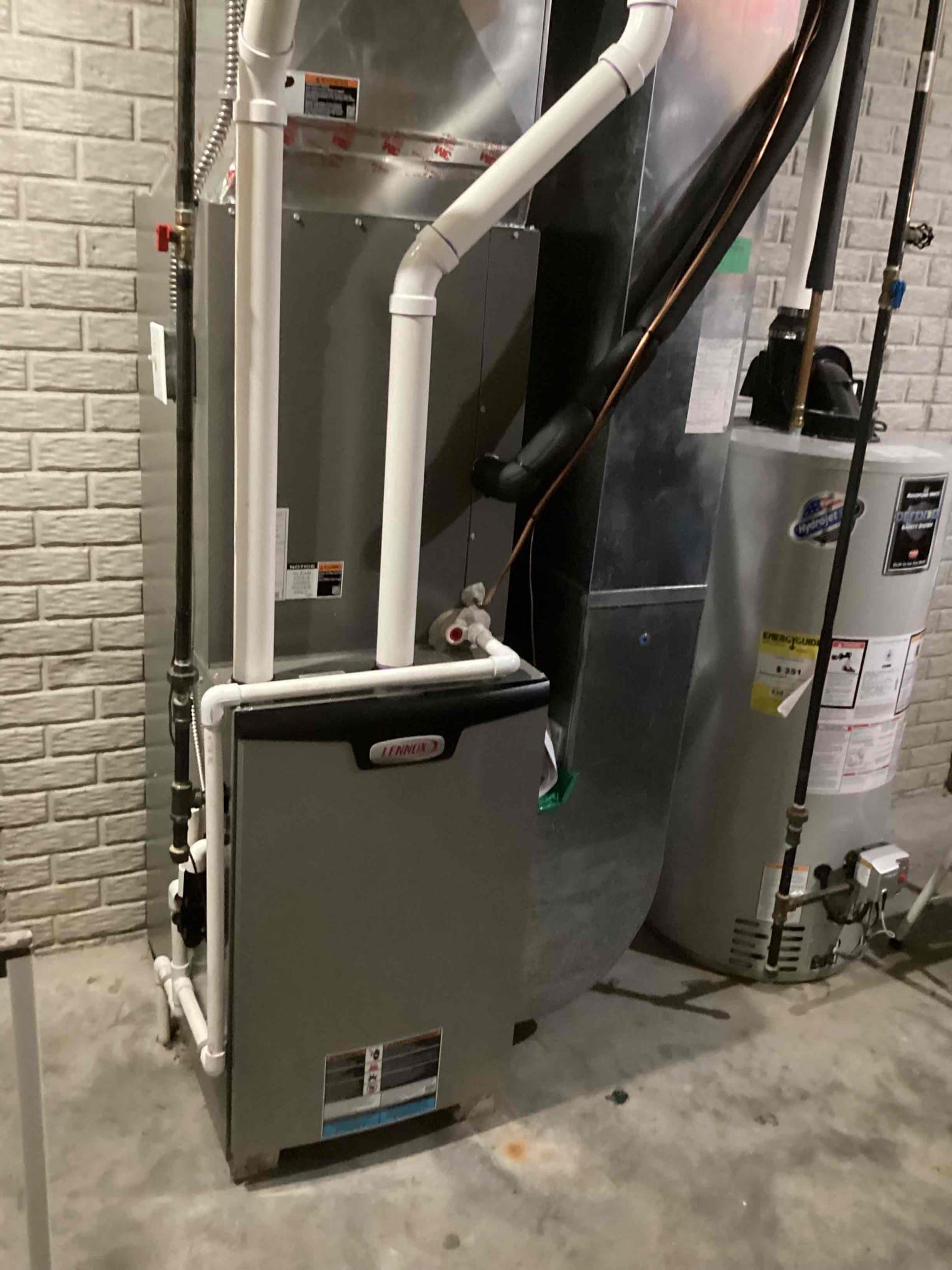A gas heater is sitting in a basement next to a water heater.