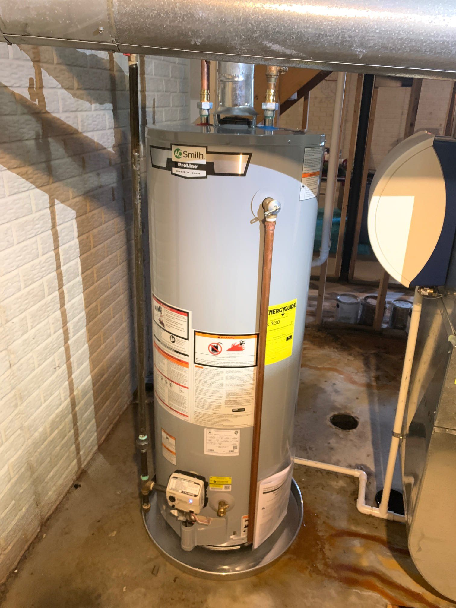 A water heater is sitting in a basement next to a staircase.