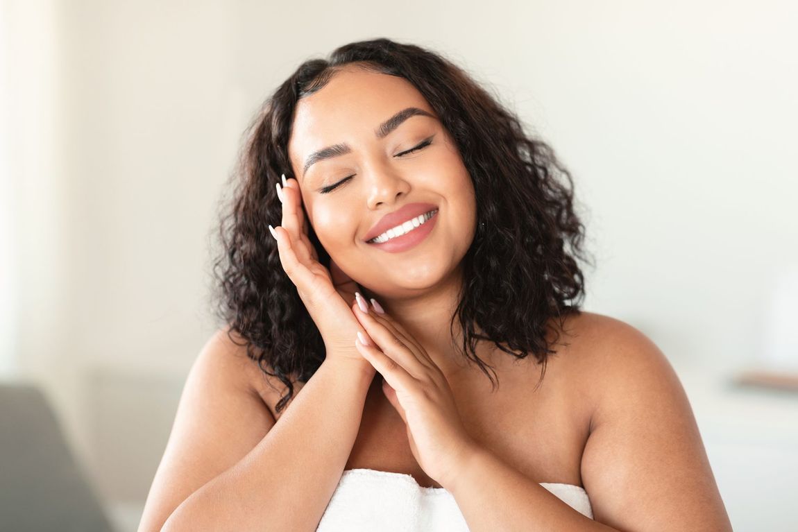 A woman is wrapped in a towel and smiling with her eyes closed.