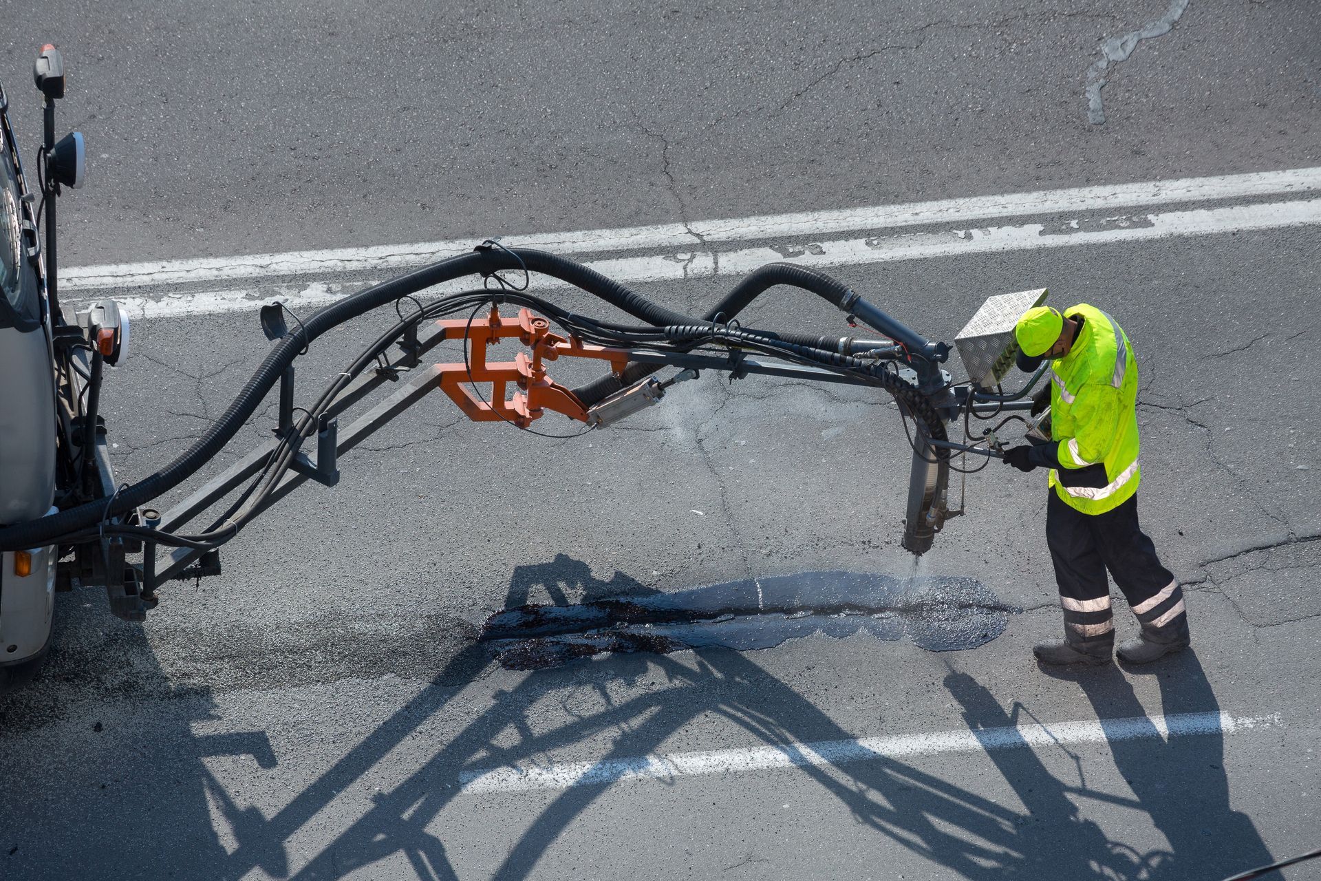 Worker in neon safety gear operating a robotic road machine on a highway. Worker in neon safety gear operating a robotic road machine on a highway.