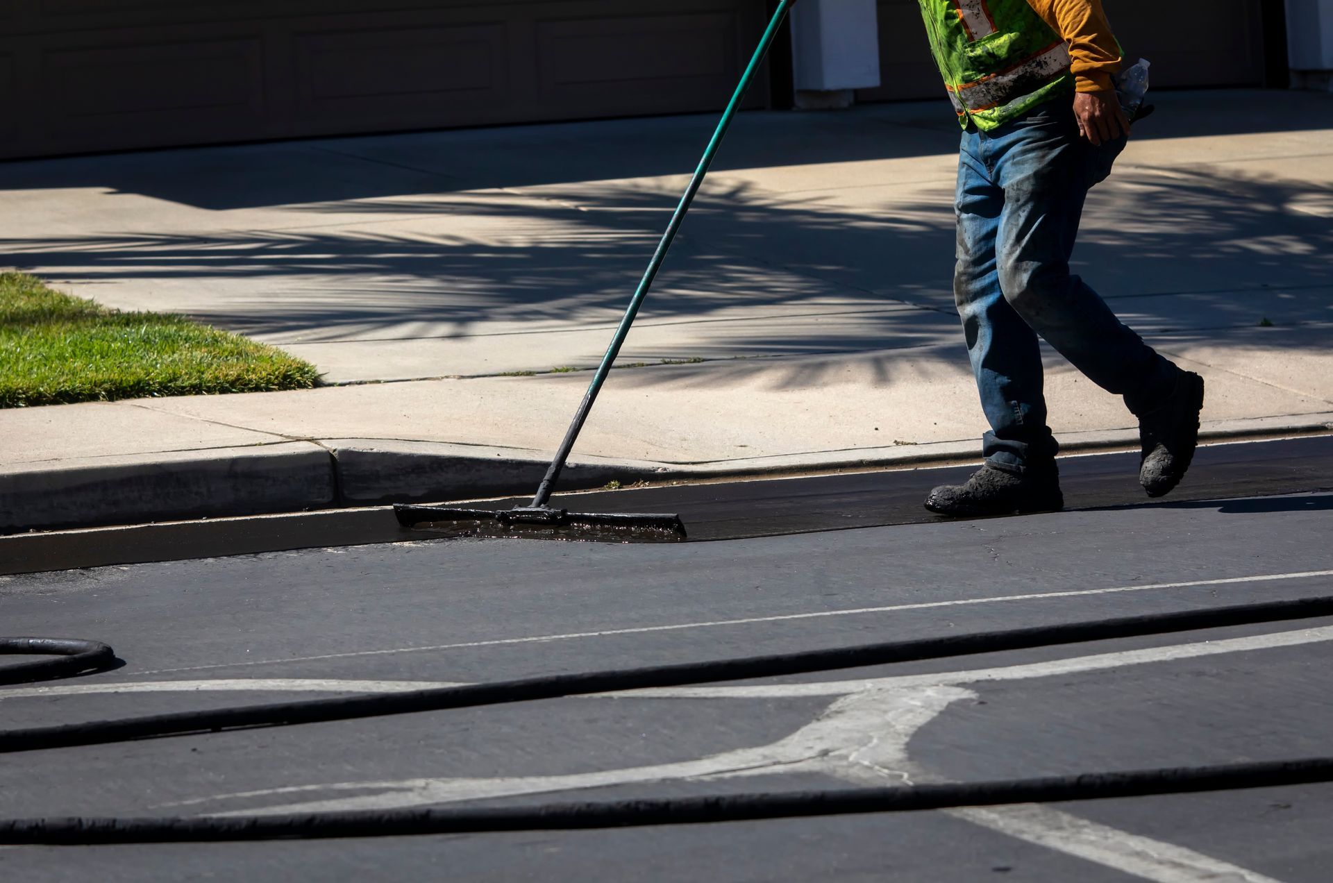 Worker sweeping a street curb with a long-handled broom near a sidewalk and grass verge