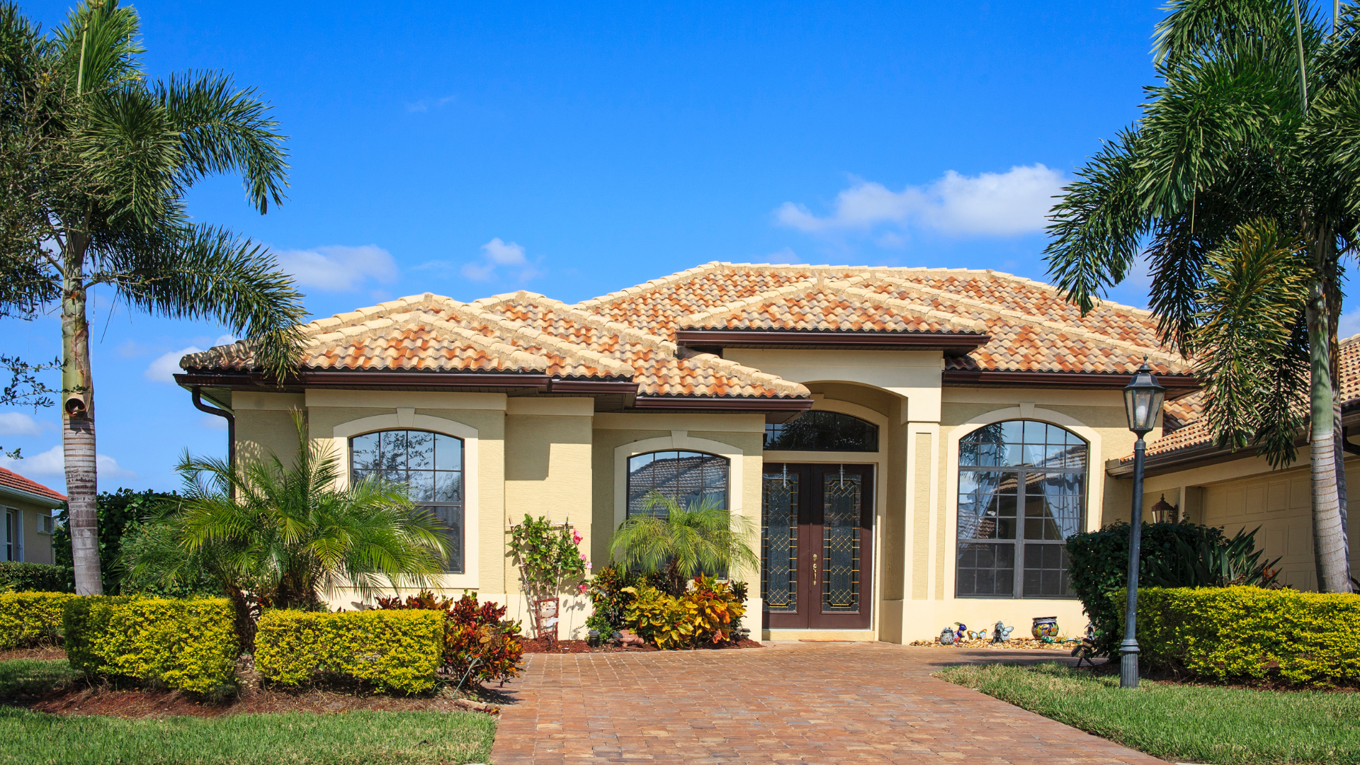 Luxurious stucco house with red tile roof, arched entryway, and landscaped front yard under a clear blue sky