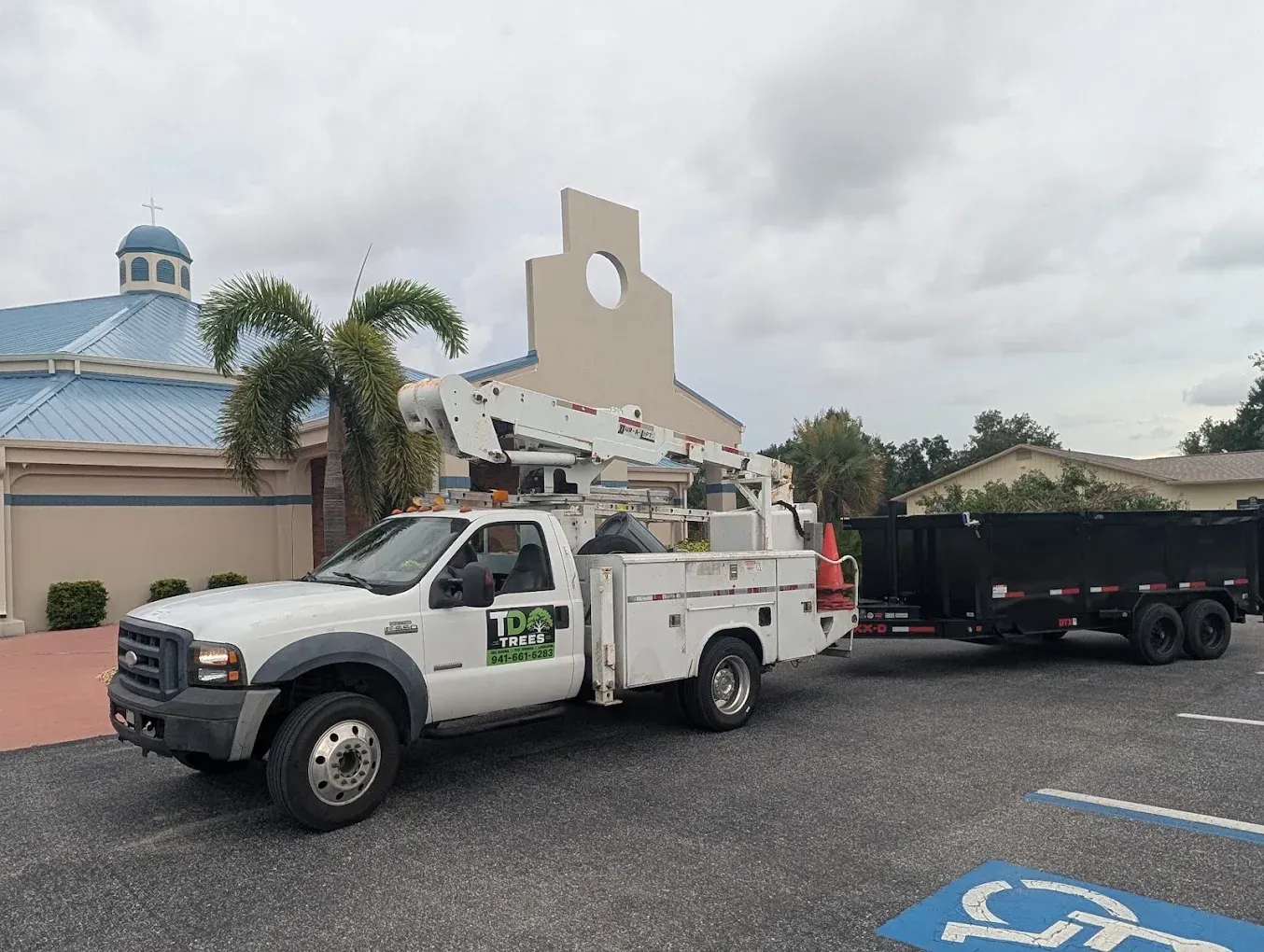 Utility truck with ladder parked beside a building, towing a black trailer in a lot