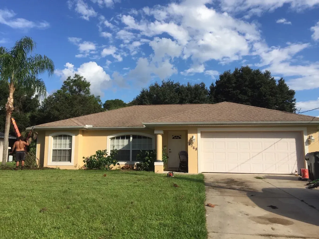 Single-story beige house with a white garage, front lawn, and driveway under a blue sky.