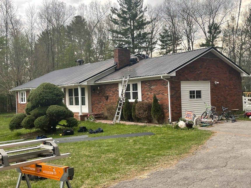 Single-story brick house with workers on the roof and ladder in the front yard