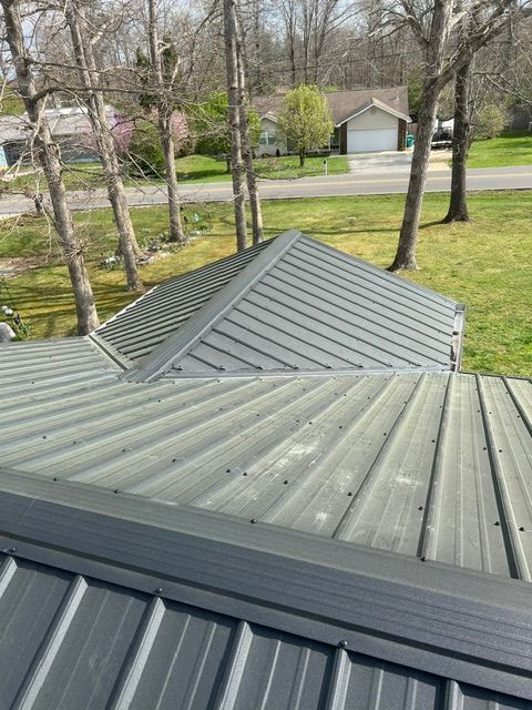 Metal roof with gray panels and a view of trees and houses in the background
