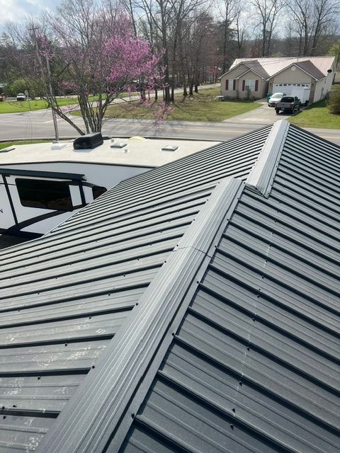 Metal roof with standing seams on a house, viewed from above with trees and neighboring homes in the background