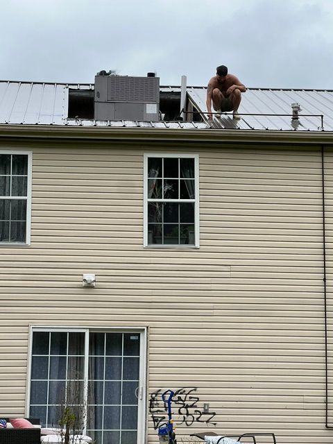Person crouches on a rooftop beside solar panels above a beige-sided house.