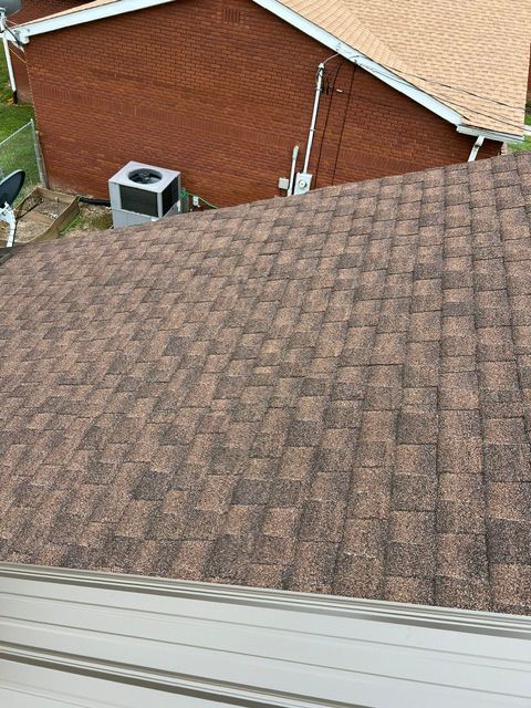 Brown shingled roof beside a red brick house, with a vent and white gutter visible.