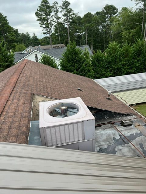 Rooftop HVAC unit on a shingled roof with surrounding metal roofing and trees in the background