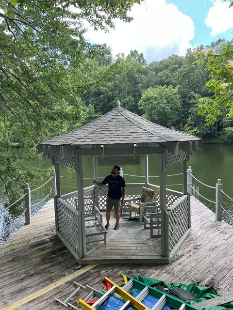 Person standing in a lakeside gazebo with rowboats and trees nearby