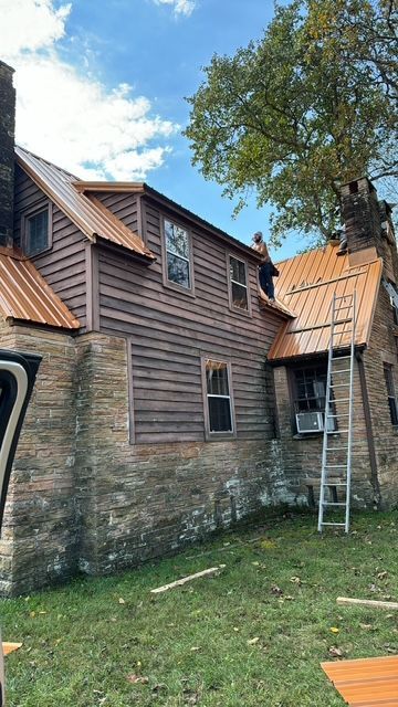 Two-story wooden house with a ladder leaning against the roof and a partly visible orange tarp on the ground