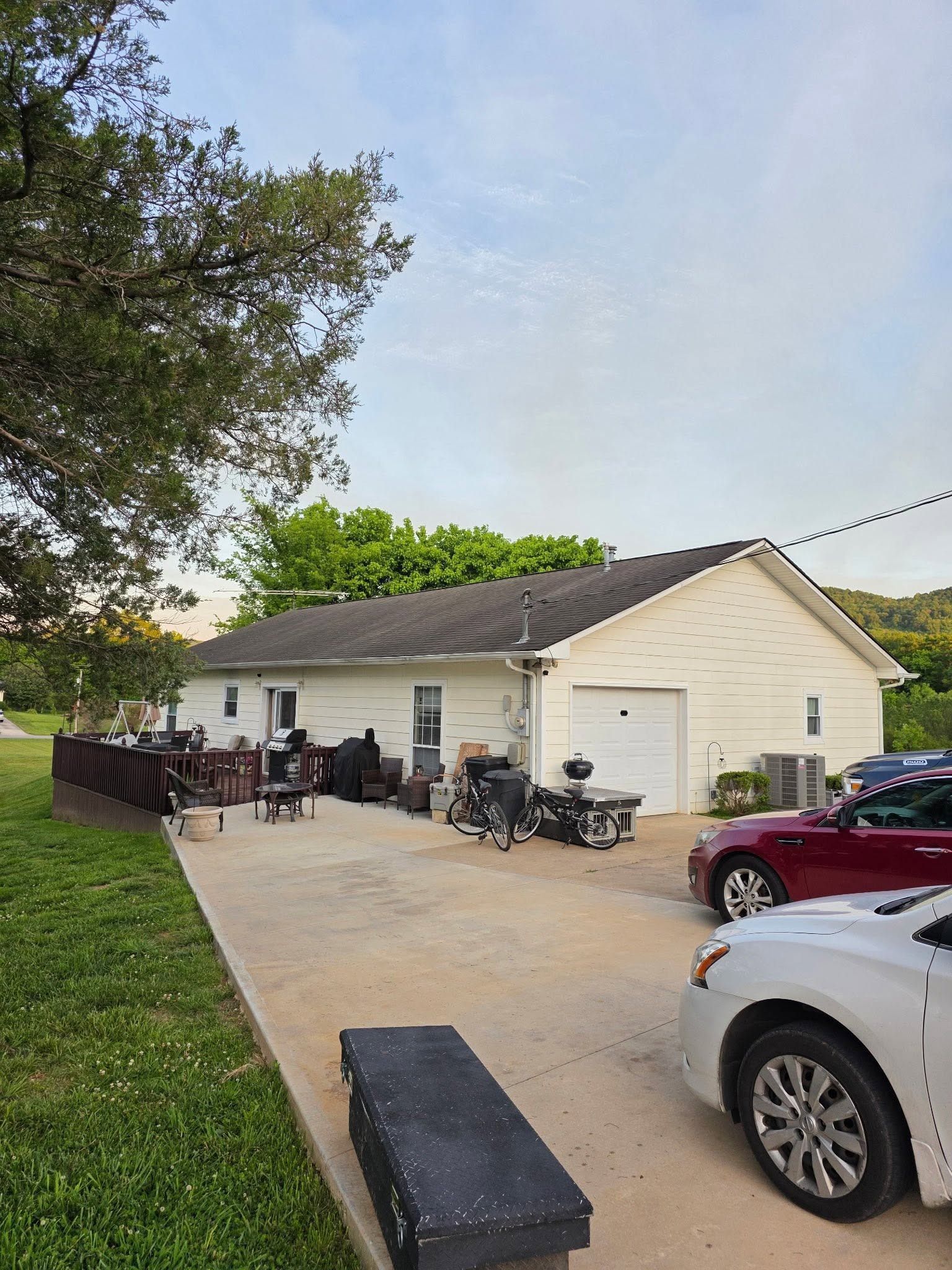Driveway beside a beige house with parked motorcycles, cars, and people on a wooden deck.