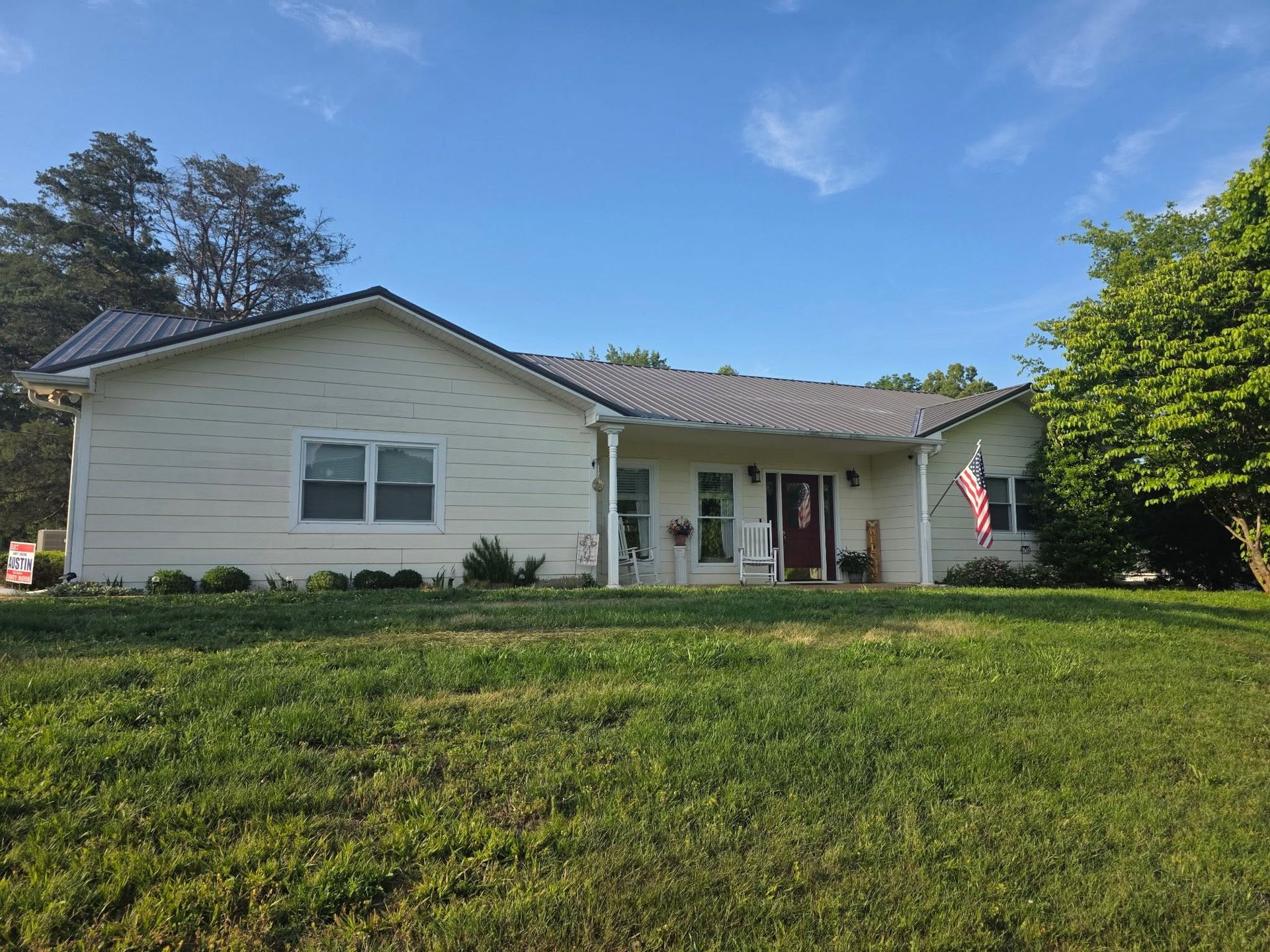 Single-story white house with a front porch and U.S. flag on a grassy lawn under a blue sky