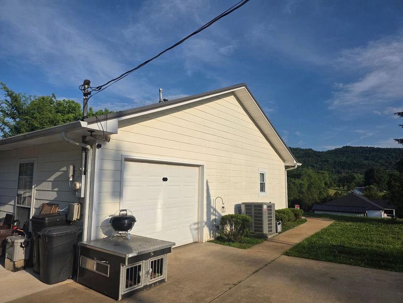 White garage with driveway, trash bins, and grill beside a grassy yard under a blue sky