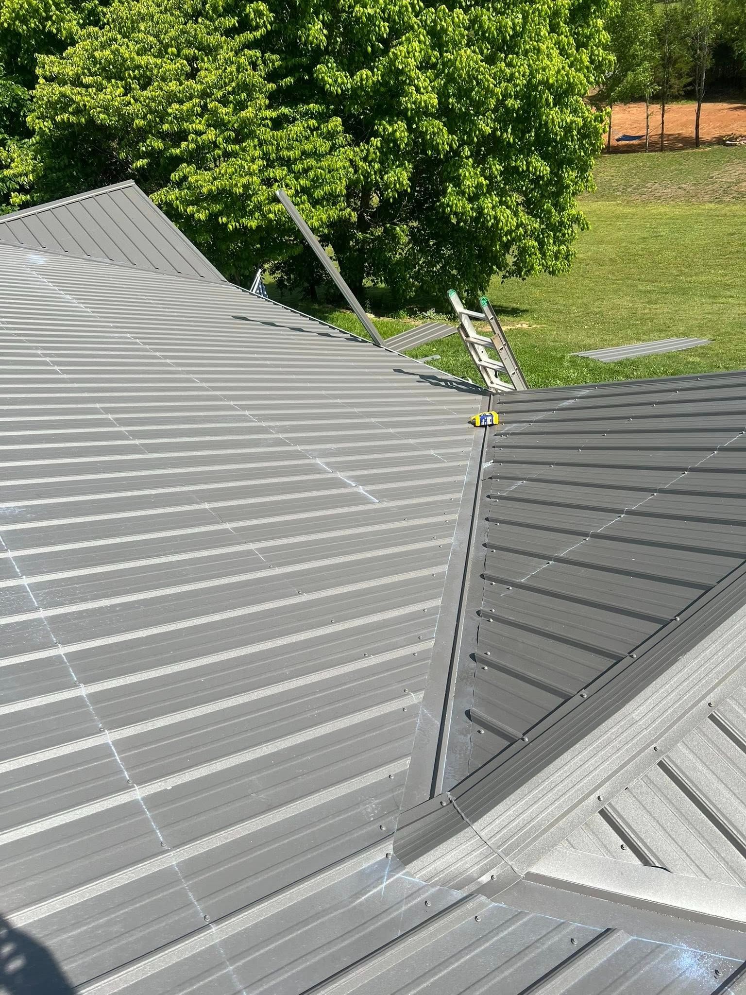 Close-up of a gray metal roof seam with a small antenna or cable bracket, with trees and grass in the background