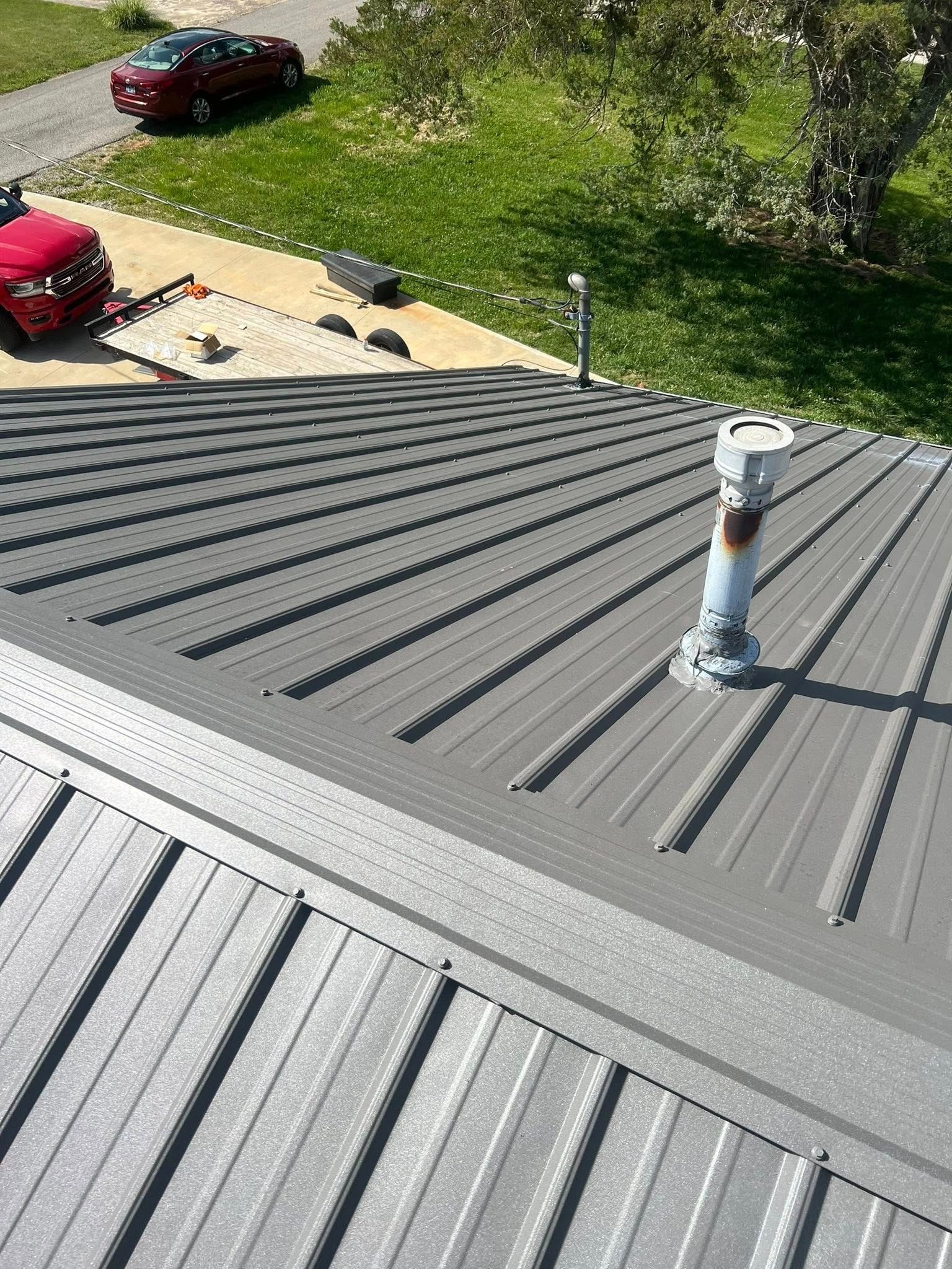 Gray metal rooftop with vent pipe, overlooking a driveway with parked cars and trees.