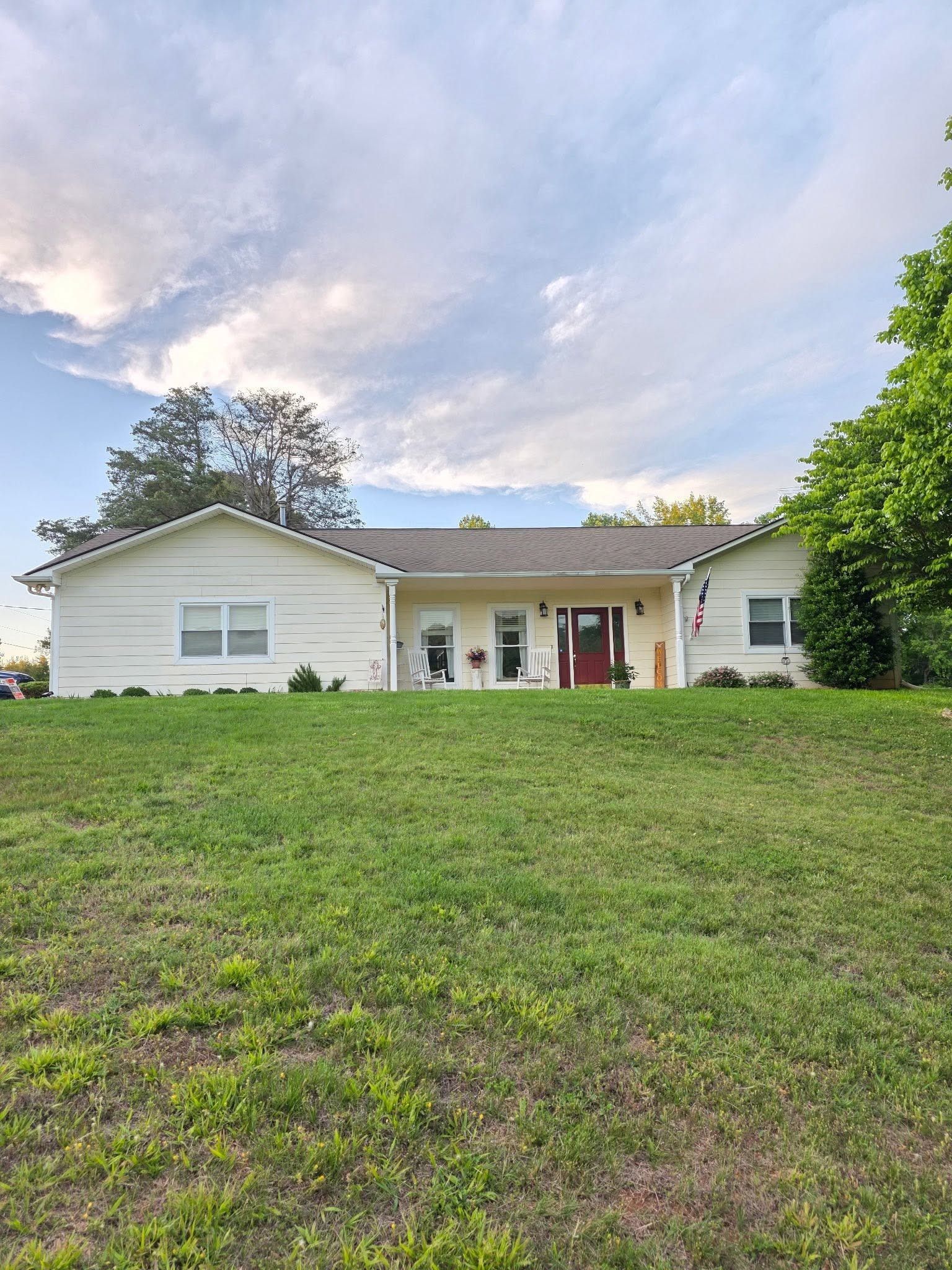 Single-story white house with a front porch and large grassy yard under a cloudy sky