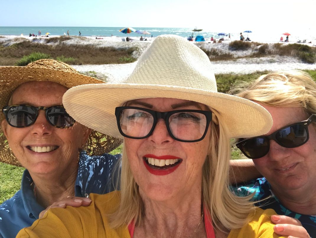 Three smiling friends in sun hats and sunglasses posing on a sunny beach