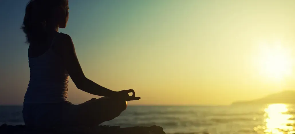 Silhouette of a person meditating by the ocean at sunset with golden light on the water
