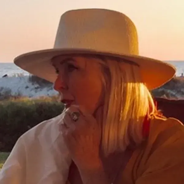 Woman in a straw hat holding flowers in a sunny garden at sunset