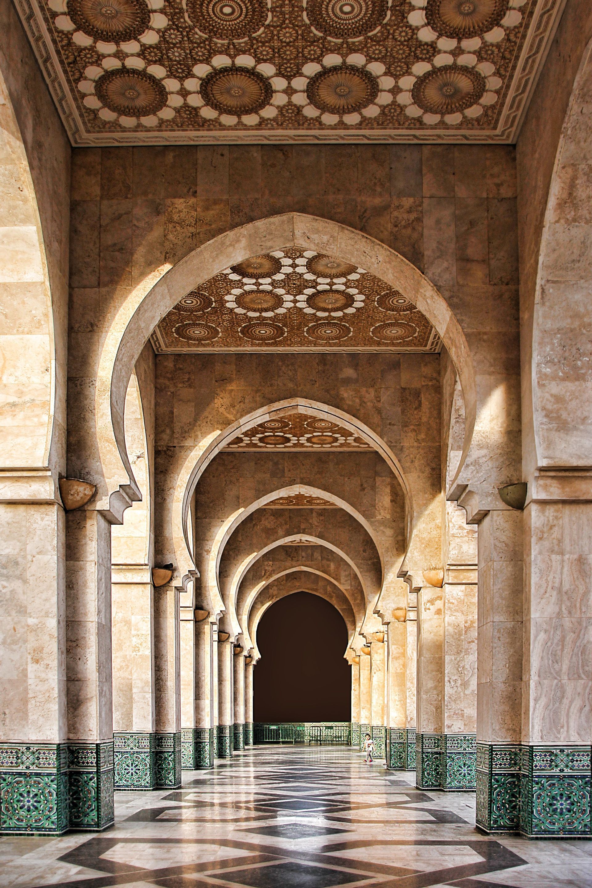 Under a bridge, concrete pillars frame a sunlit patch of tall grass behind a stone barrier.