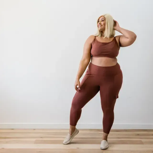 Person in mauve athletic wear posing in a bright room with a white wall and wooden floor.