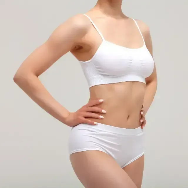 Woman in white sports bra and briefs posing against a plain gray background.