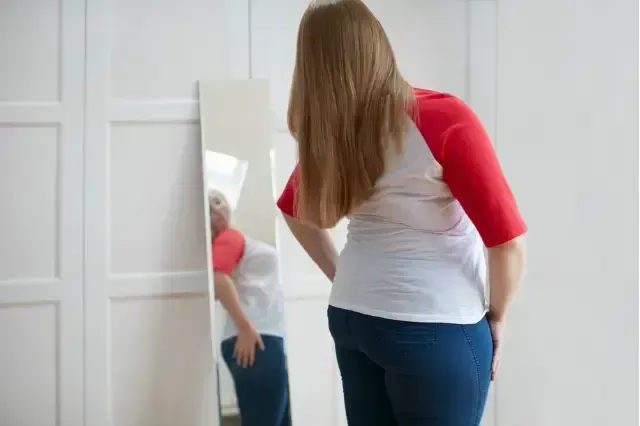 Person standing in front of a mirror, examining the back of a white and red shirt