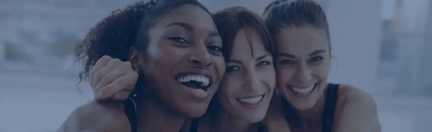 Three smiling friends posing closely together outdoors on a beach or waterfront.