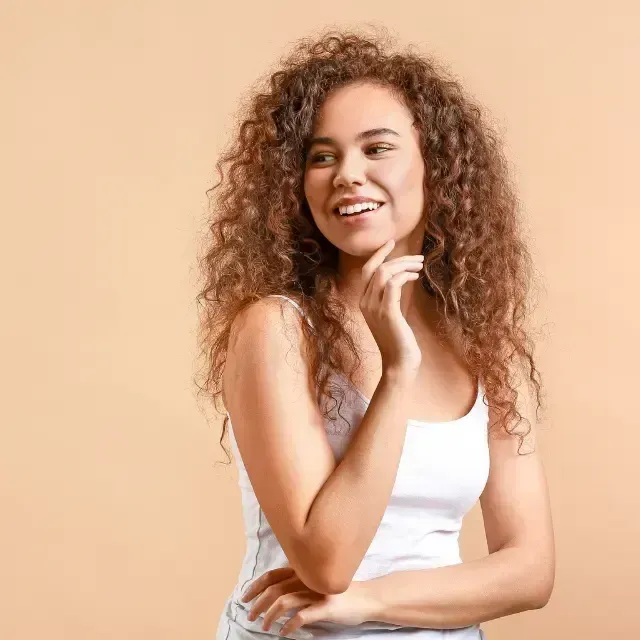 Smiling curly-haired woman in a white top posing against a peach background