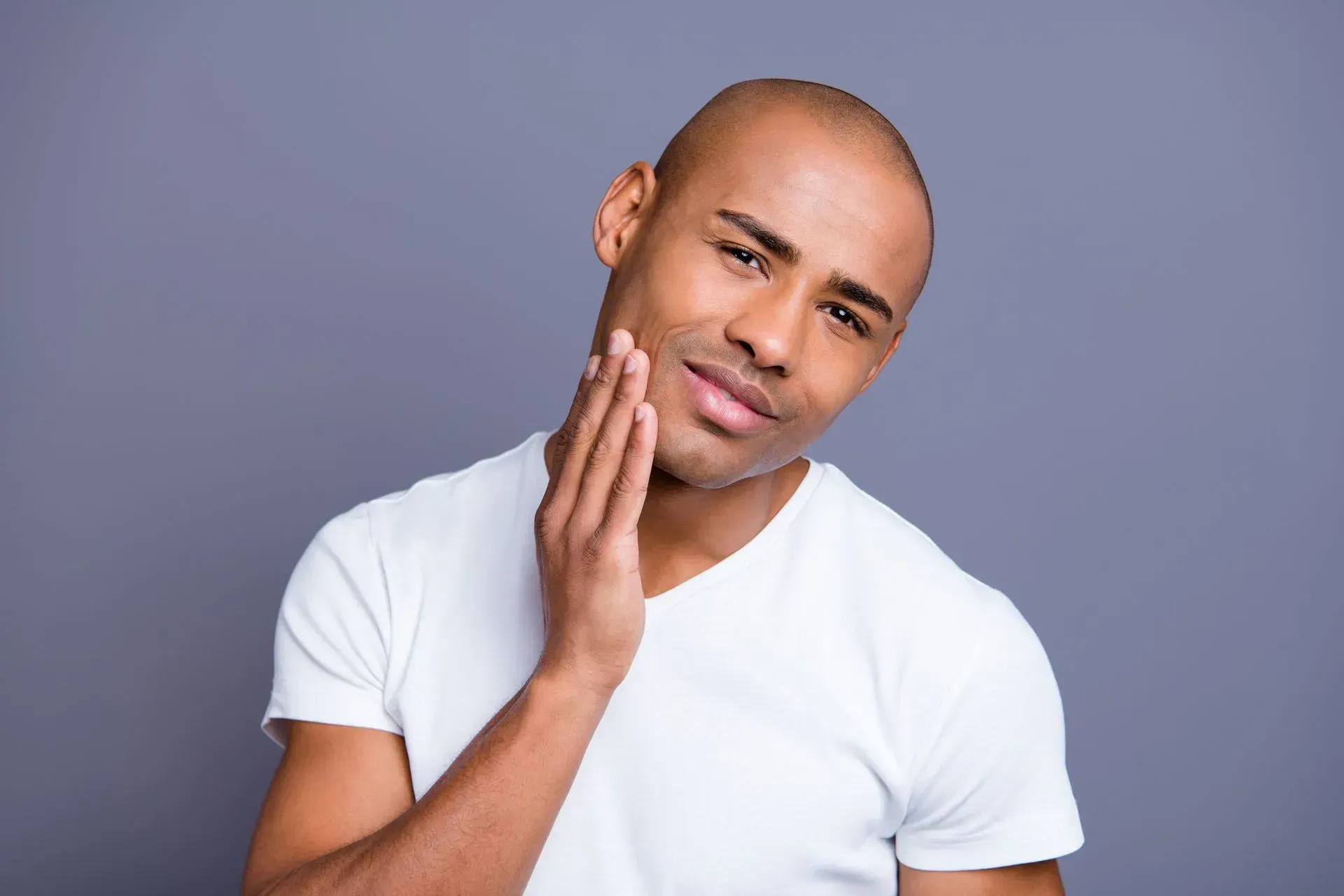 Man touching his cheek with a slight smile against a gray background