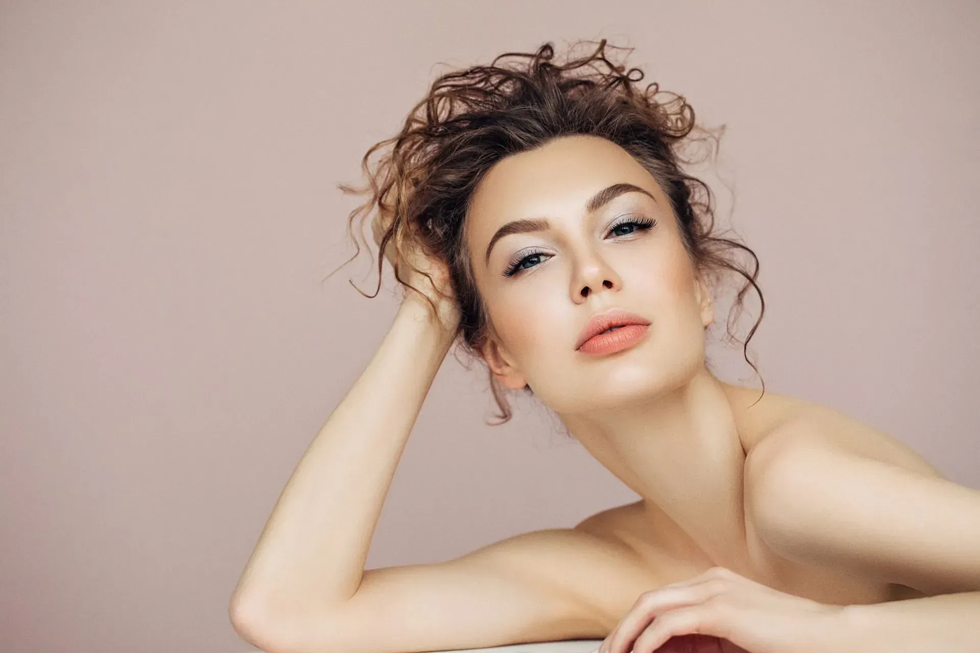 Portrait of a woman with curly hair posing against a soft pink background