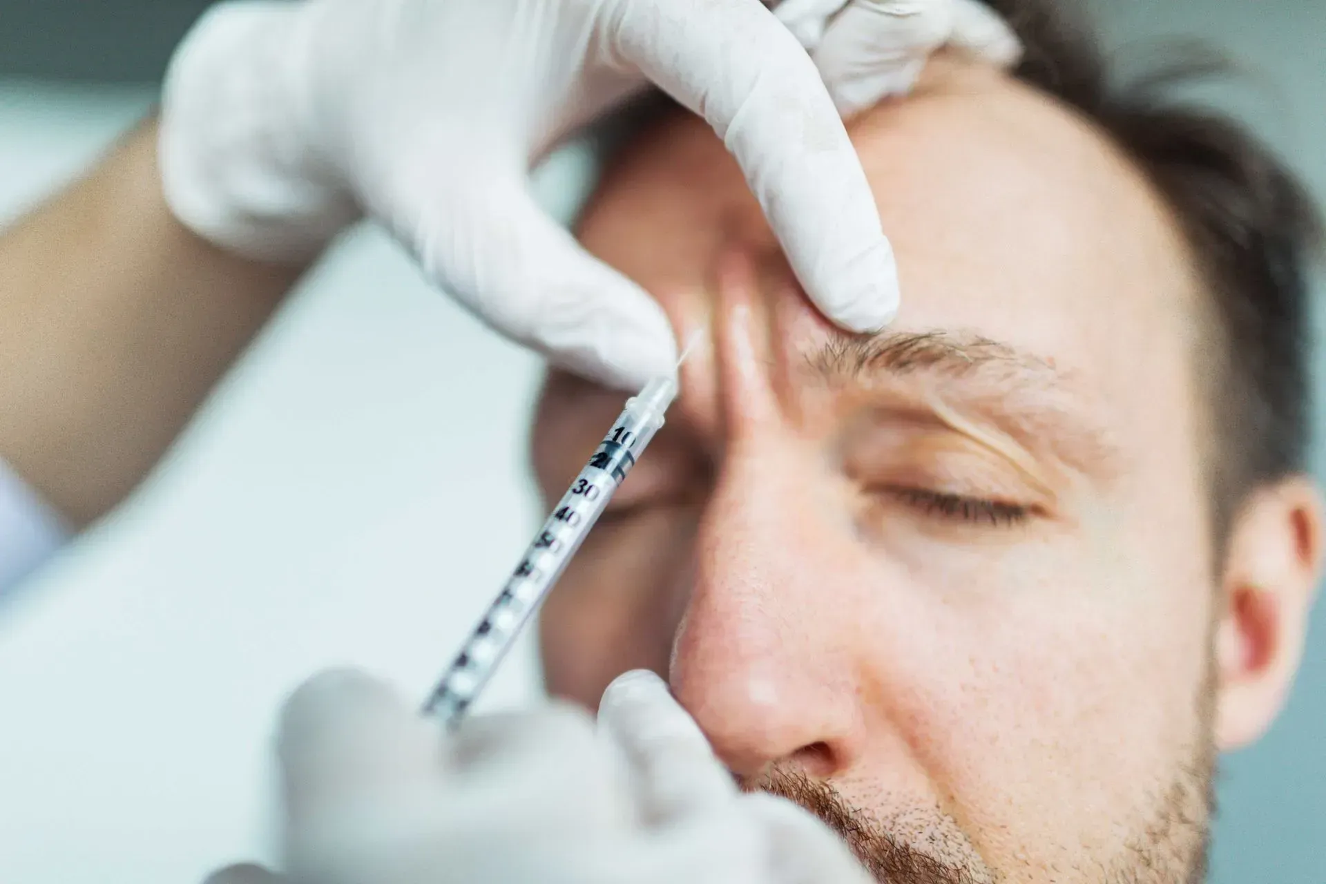 Hand gloved clinician injects eyebrow area of a patient during cosmetic procedure