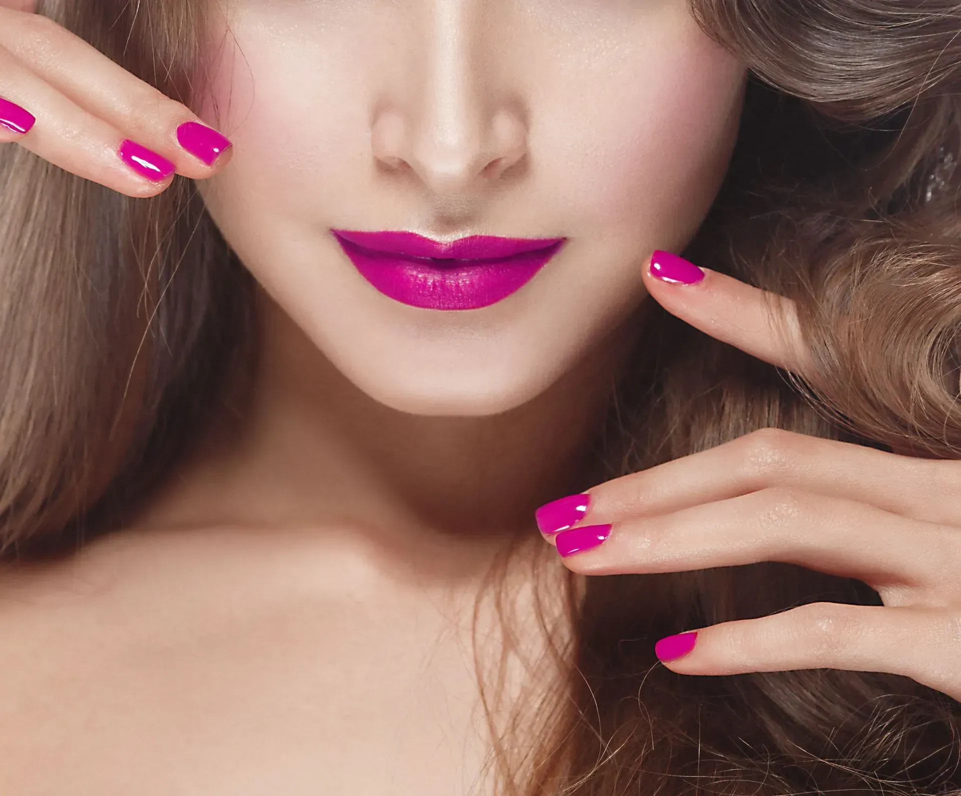 Close-up of a woman’s face with glossy pink lips and manicured hands framing it.