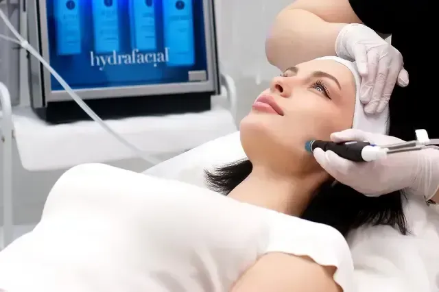 Woman receiving facial treatment with a handheld device in a spa clinic, lying on a treatment bed
