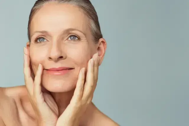 Smiling woman gently touching her face against a light blue background