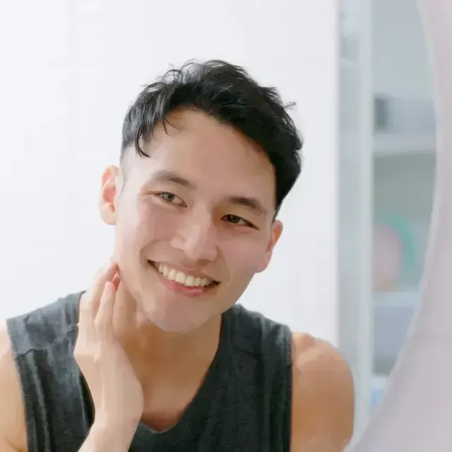 Smiling person in a black tank top, touching their neck in a bright indoor setting
